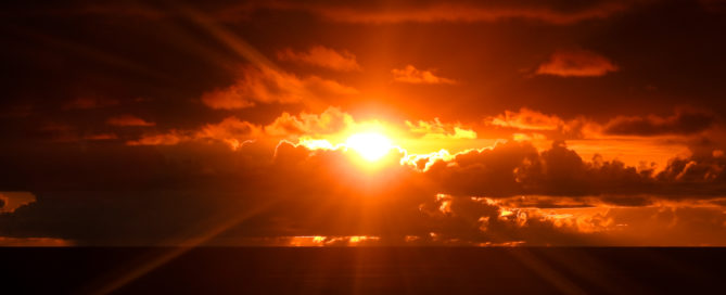 A photo of a fiery orange Hawaiian sunset with fluffy clouds partially obscuring the sun.