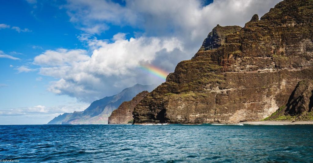 A photo of a vibrant rainbow arcing over the dramatic cliffs and lush green valleys of the Napali Coast on Kauai.