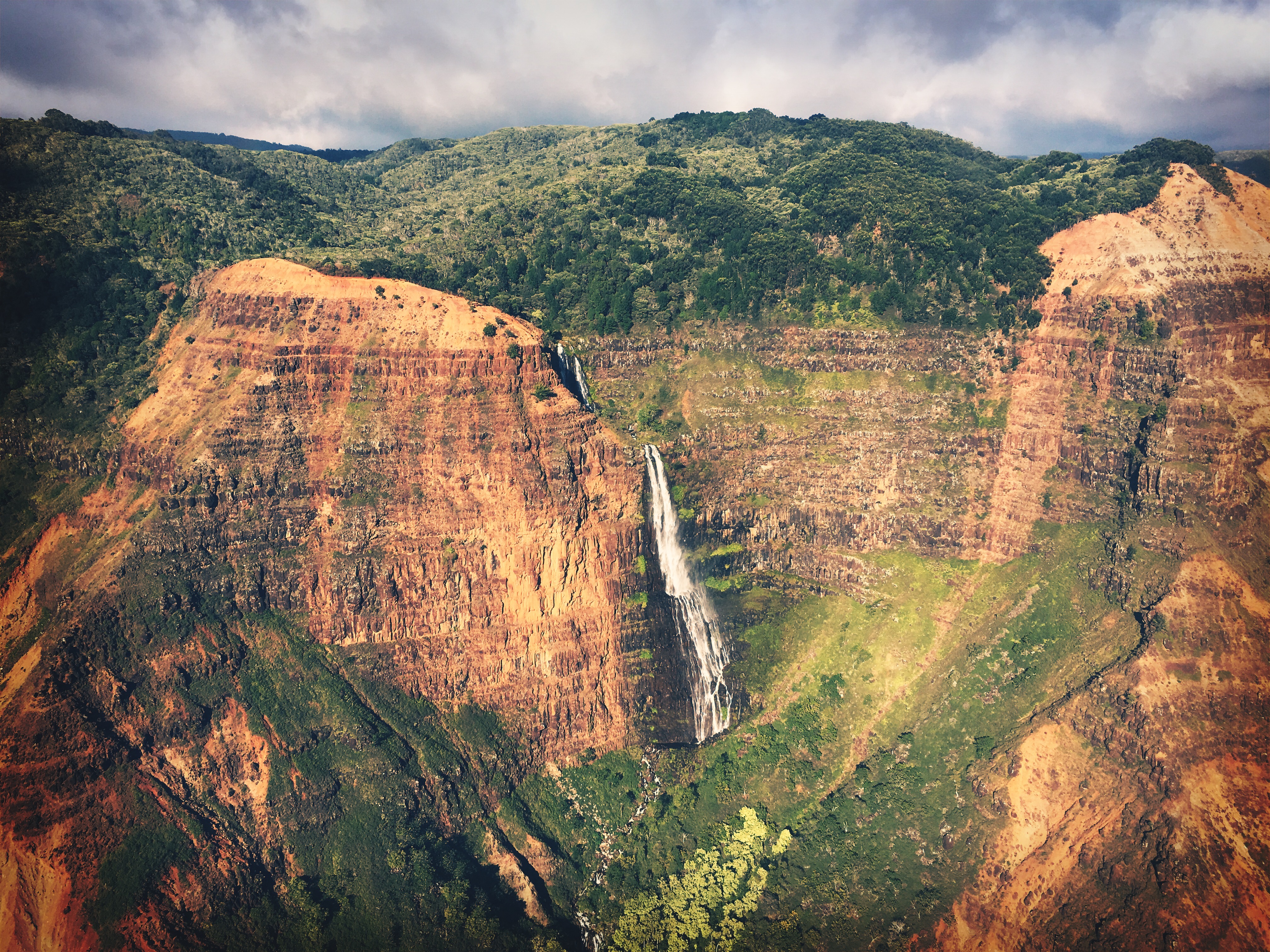 Aerial view of Kauai waterfall cascading into a lush green pool.