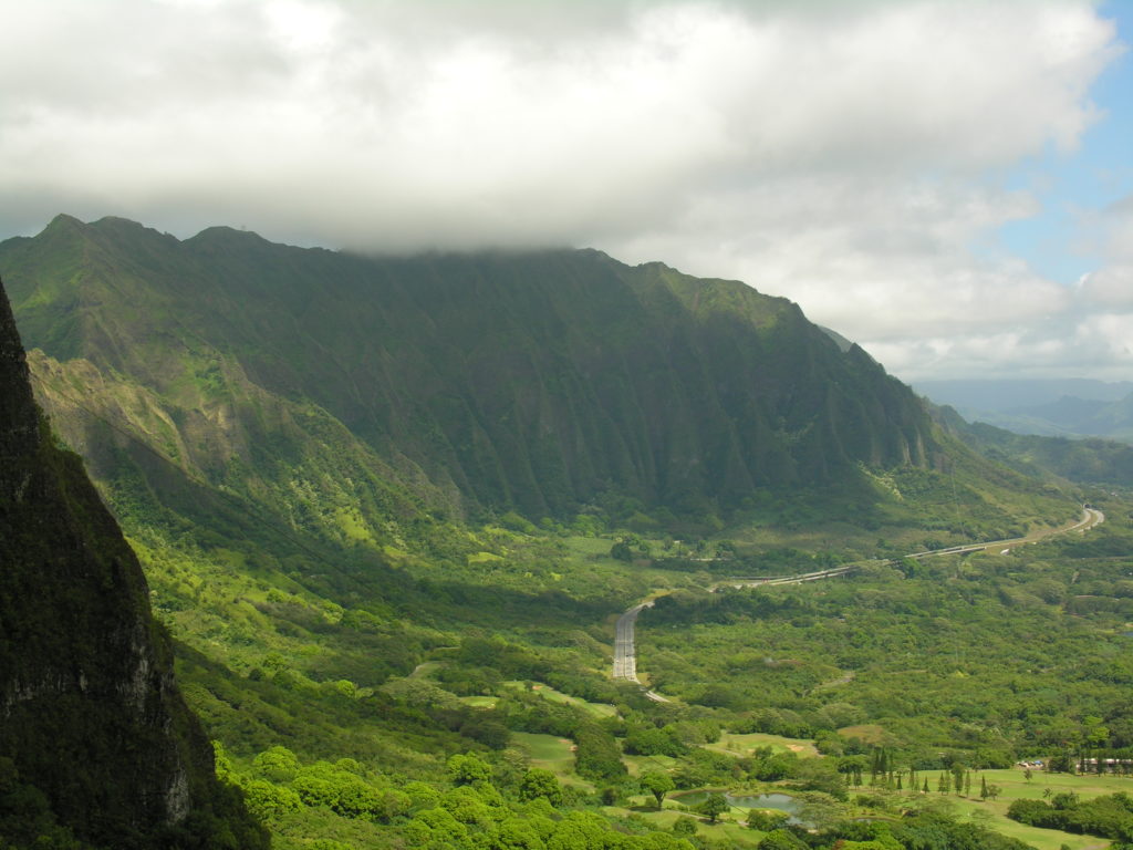 A scenic view of the Koʻolau Mountains from Nuuanu Pali Lookout on Oahu, Hawaii, with lush green valleys and the winding Pali Highway below.