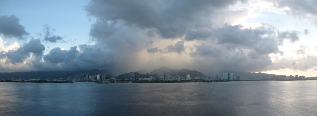 A photo of Honolulu with rain clouds gathering overhead and choppy waves on the shore.