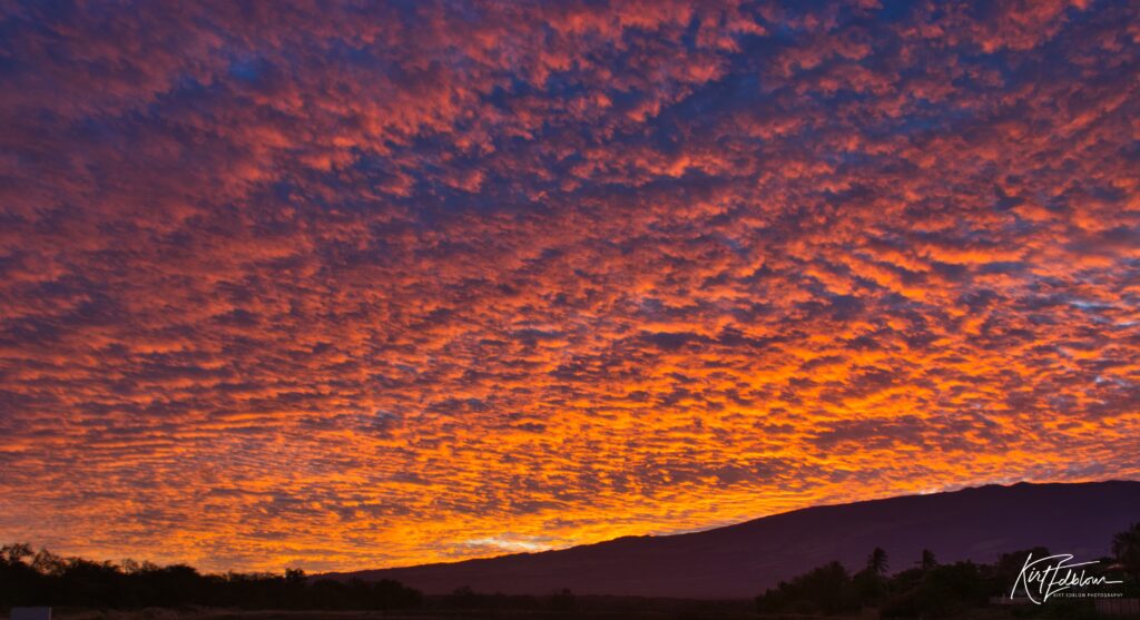 A photo of a fiery orange Hawaiian sunset with fluffy clouds above the mountains.