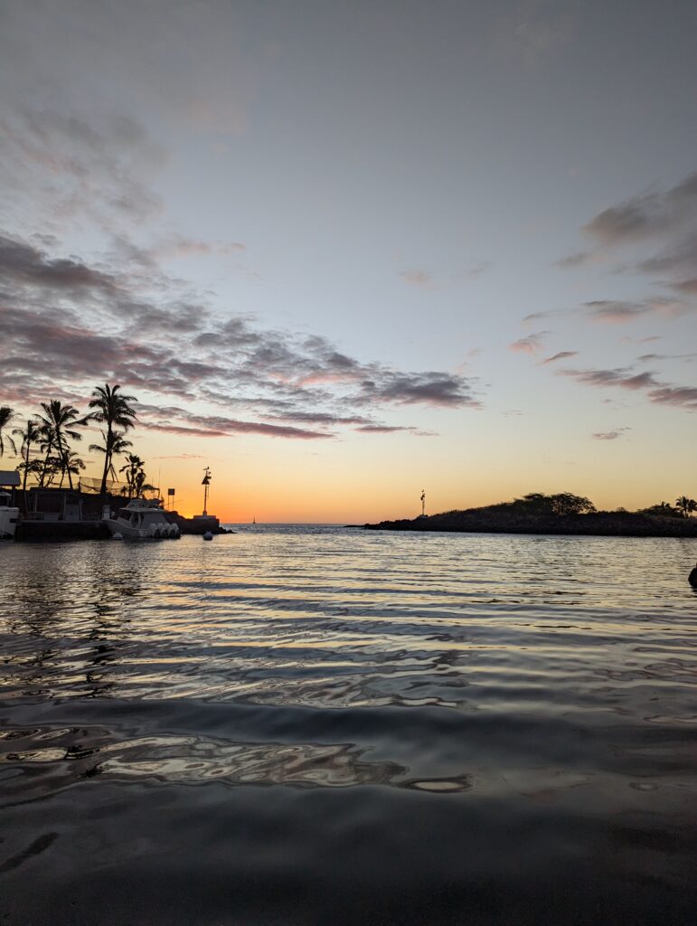 A photo of Honokohau Boat Harbor in Kailua-Kona at twilight, with the sky ablaze in colorful hues.