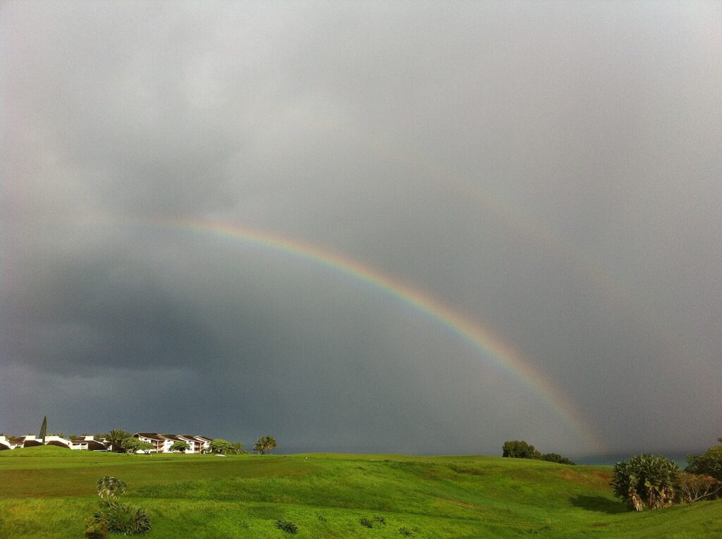 Rainbow over Princeville, Kauai — tropical homes and green hills beneath bright North Shore skies. 